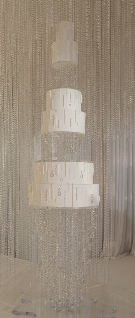 Nine-foot white cake with hand-hung glass bead curtains on a custom acrylic stand by Nilani