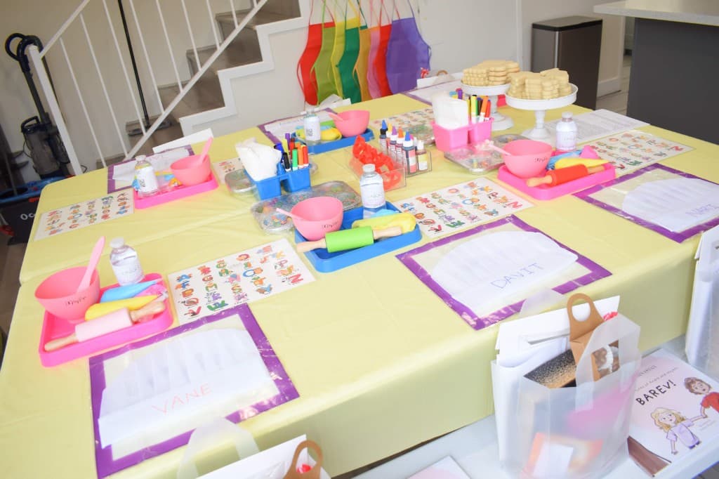 Kids class table with chef hats, cookies on stands, aprons on the wall, and goodie bags